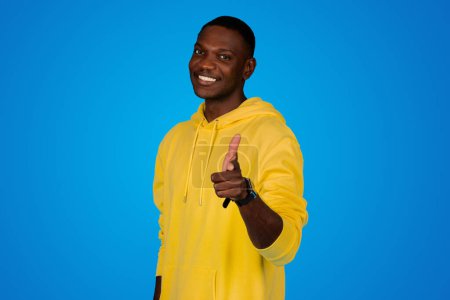 Photo for Smiling glad young black guy point fingers at camera, isolated on blue background, studio. Recommendation ad and offer, human emotions, your choice, your turn, motivation lifestyle - Royalty Free Image