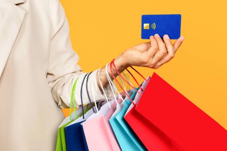 Photo for Young asian woman hold many bags on hand, shows credit card, isolated on yellow studio background, cropped. Sale, finance and shopping recommendation, ad and offer, pay and buy purchases - Royalty Free Image