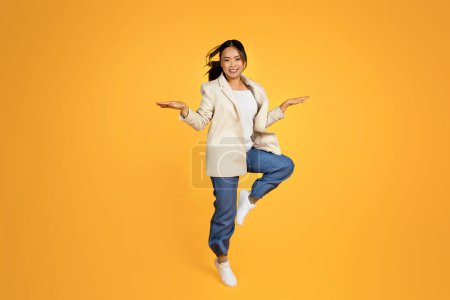 Photo for Cheerful young asian woman in jacket jumping, freezes in air, have fun, enjoy great mood, free time, isolated on yellow studio background. Good news, people emotions, lifestyle - Royalty Free Image