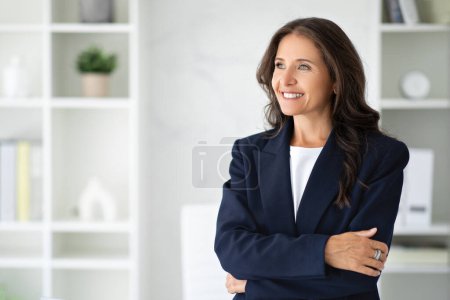 Confident smiling beautiful brunette long-haired middle aged woman in forma outfit manager posing at white modern office, looking at copy space. Career, job opportunities in 50s concept