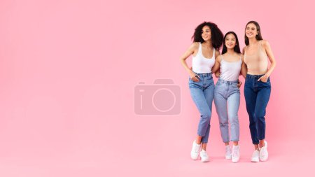 Foto de Retrato de tres jóvenes amigas diversas abrazando y posando aisladas sobre fondo de estudio rosa, panorama con espacio libre, pancarta, longitud completa - Imagen libre de derechos