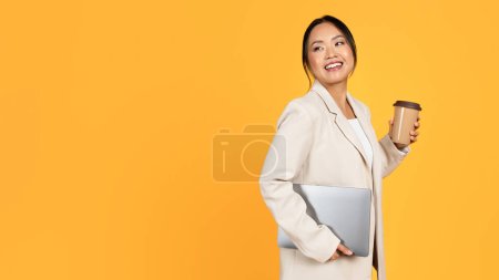 Photo for Happy young asian woman in suit with cup of takeaway coffee and laptop looking at empty space, isolated on yellow studio background. Professional work, lifestyle, device, ad and offer - Royalty Free Image