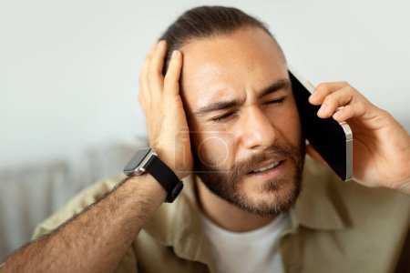 Photo for Closeup of millennial man in pain touching his head and calling doctor or ambulance on phone, suffering from migraine, copy space. Young guy have phone conversation, hear bad news - Royalty Free Image