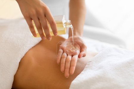 Photo for Unrecognizable Masseur Woman Pouring Oil On Hand, Doing Body Care Massage Procedure For Client Lady At Spa Wellness Center Indoor, Cropped Closeup Shot. Massage Cosmetics Concept - Royalty Free Image