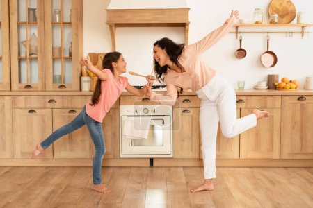 Photo for Happy European Mom And Daughter Kid Dancing And Singing With Spoons In Kitchen Interior. Full Length Shot Of Mother And Little Girl Fooling And Having Fun Together At Home - Royalty Free Image