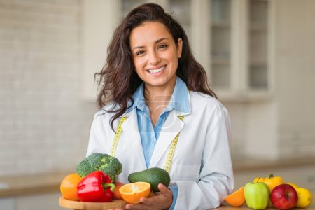 Téléchargez les photos : Portrait de femme nutritionniste souriante avec assiette de fruits frais, travaillant à la clinique de perte de poids, posant et souriant à la caméra. Consultant en nutrition saine recommandant une alimentation saine - en image libre de droit