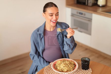 Foto de Mujer embarazada europea feliz saboreando pasta casera, disfrutar de comer espaguetis, sentarse a la mesa en el interior de la cocina en casa, por encima de la vista, espacio libre - Imagen libre de derechos