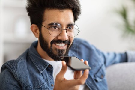 Photo for Young Smiling Indian Man Using Recording Voice Message On Smartphone, Handsome Millennial Eastern Guy Using Modern Mobile Phone, Browsing Virtual Assistant Or Speaking With Loudspeaker Mode, Closeup - Royalty Free Image