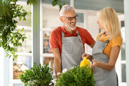 Photo for Happy Senior Man And Woman In Aprons Watering Flowers And Chatting, Smiling Mature Couple Tending To Plants At Terrace Of Their Country House, Older Spouses Enjoying Retirement Time, Copy Space - Royalty Free Image
