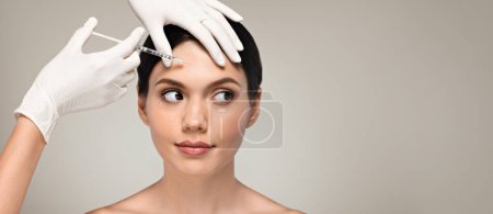 Photo for Hands of cosmetologist in gloves make rejuvenating anti wrinkle injection to calm millennial european woman, isolated on gray studio background. Beauty care, cosmetic procedures with professional - Royalty Free Image