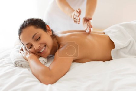 Foto de Primer plano de la joven feliz con los ojos cerrados teniendo sesión de masaje en el salón de spa, disfrutando del cuidado corporal y la relajación en el centro de belleza interior. Tratamientos de Mimos y Bienestar - Imagen libre de derechos
