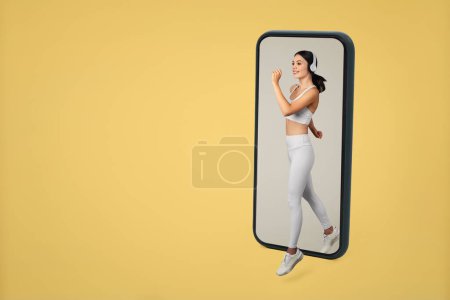 Photo for Fitness application. Sporty woman running from cellphone screen, having online cardio workout over yellow studio background, free space. Sport and technology concept - Royalty Free Image
