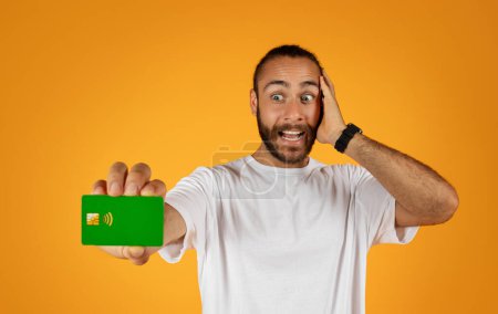 Photo for Glad surprised adult european guy with beard put hand to face, show credit card isolated on orange studio background. Win finance, profit, ad and offer, savings and cash, people emotions - Royalty Free Image