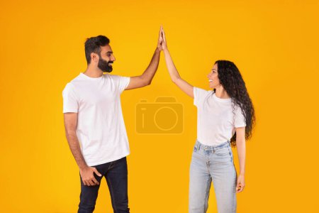 Téléchargez les photos : Joyeux couple arabe jeune donnant High Five à l'autre célébrant le succès commun sur fond jaune, debout dans le studio jouissant du travail d'équipe, heureux de la réussite familiale et de la victoire - en image libre de droit
