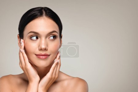 Photo for Calm millennial european woman with perfect glowing skin touching hands to face, enjoy routine procedures, isolated on gray studio background, close up. Basic nude makeup, beauty, skin care - Royalty Free Image