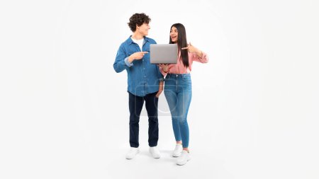 Photo for Online Offer. Students Young Couple Holding Laptop Together And Pointing Fingers At Computer Gadget, Recommending Website For E-Learning Over White Studio Background. Panorama - Royalty Free Image
