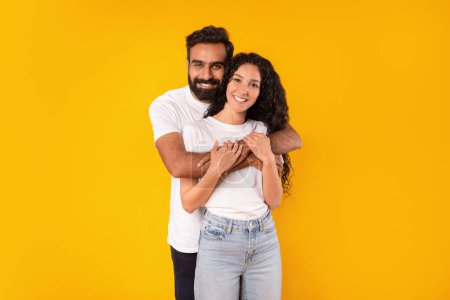 Téléchargez les photos : Studio Shot Of Smiling Romantic Arab Couple Embrassant sur fond jaune, aimant jeune homme étreignant sa femme heureuse debout derrière son dos, souriant à la caméra ensemble. Relation et amour - en image libre de droit