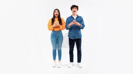 Photo for Great Mobile Offer. Joyful Young Couple Using Cellphones Posing With Opened Mouth, Excited About New Phone Application Standing Over White Studio Background. Full Length Shot, Panorama - Royalty Free Image