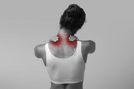 Photo for Neck pain muscle stress and strain. Unrecognizable stressed woman wearing white top massaging red sore neck highlighted in red, back view, black and white photo, copy space - Royalty Free Image