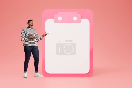 Photo for Glad adult black woman in casual with open mouth point fingers at big plan with empty space, has fun, isolated on pink studio background. Day planning, motivation, success and win - Royalty Free Image