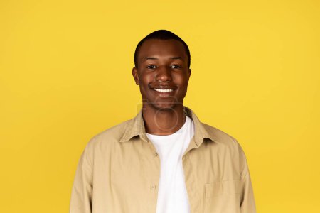 Foto de Imagen de un chico afroamericano milenario sonriente en un estudio casual y aislado de color amarillo. Emociones humanas, videollamada, anuncio y oferta, estilo de vida y comunicación remota - Imagen libre de derechos