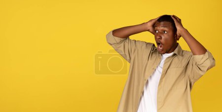 Photo for Shocked excited scared millennial african american guy with open mouth presses hands to head, look at empty space, isolated on yellow background. Surprise reaction, emotions, ad and offer, sale - Royalty Free Image