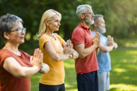 Photo for Outdoor Yoga. Group Of Happy Senior People Meditating Together, Diverse Smiling Older Men And Women In Activewear Standing With Clasped Arms, Practicing Yoga, Enjoying Healthy Lifestyle, Side View - Royalty Free Image
