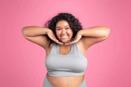 Foto de Feliz sonrisa de gran tamaño mujer negra en ropa deportiva sobre fondo rosa, entrenamiento y posando en la cámara. Imperfección corporal, aceptación corporal, concepto positivo corporal - Imagen libre de derechos