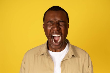 Photo for Unhappy despaired millennial african american guy in casual with open mouth, screaming, isolated on yellow studio background. Depression, stress, fear human emotions, bad news reaction - Royalty Free Image