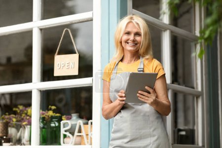 Photo for Beautiful Mature Woman With Digital Tablet Standing At Terrace Near Eco-Cafe, Happy Older Female Small Business Owner Using Modern Gadget And Smiling At Camera, Making Online Shopping - Royalty Free Image
