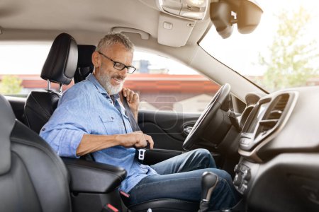 Photo for Safety driving concept. Handsome senior man driver fasten seat belt in car. Positive elderly gentleman sitting inside nice automobile, going to market, travelling alone, side view - Royalty Free Image