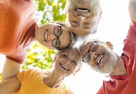 Photo for Group portrait of happy senior friends looking down at the camera while standing together outdoors, smiling active older people posing in huddle after group yoga training in park, low angle shot - Royalty Free Image
