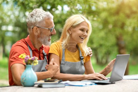 Photo for Happy Mature Spouses Shopping Online On Laptop While Sitting Outdoors In Their Garden, Smiling Older Couple Wearing Aprons Purchasing In Internet, Using Modern Technologies On Retirement, Free Space - Royalty Free Image