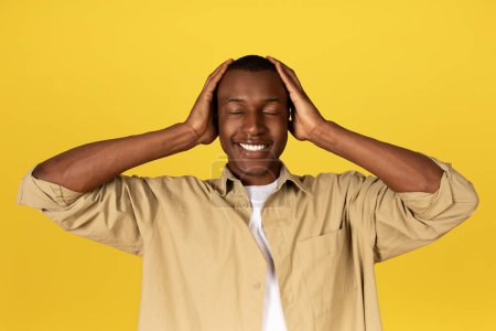 Photo for Glad millennial african american guy in casual with closed eyes, covers ears with hands, isolated yellow studio background. Human emotions, ad and offer, silence, do not hear - Royalty Free Image