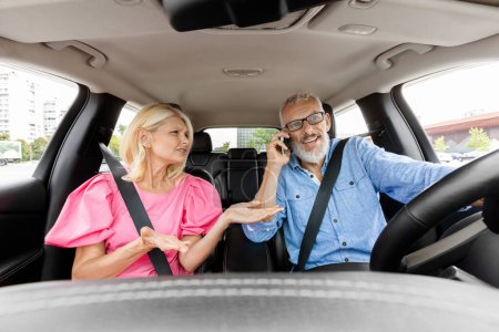 Photo for Angry stressed senior woman gesturing and shouting while her husband boyfriend man the car driver talking on mobile phone and losing concentration. Dangerous driving and gadgets - Royalty Free Image