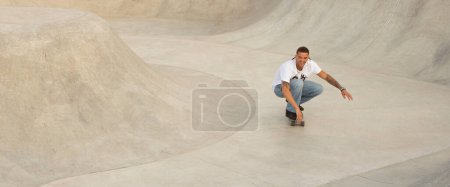 Téléchargez les photos : Jeune homme européen à l'extérieur au skate park, chevauche habilement son skateboard, exécutant des tours complexes avec facilité, panorama, espace libre. Son agilité incarne l'esprit de la culture du skateboard urbain - en image libre de droit