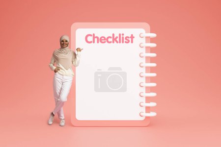 Photo for Happy confident young arab woman in casual and hijab point finger at checklist with empty space, isolated on pink studio background. Day planning, motivation, do it recommendation - Royalty Free Image