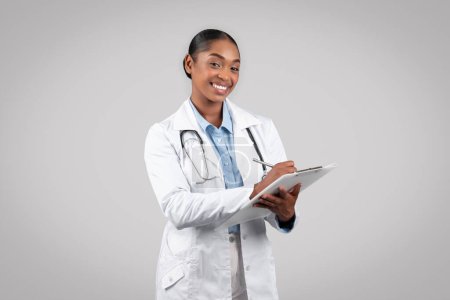 Photo for Professional confident black woman doctor in white coat, writing prescription, examination, healthcare, isolated gray background studio. Medical help at clinic, work, professional occupation - Royalty Free Image