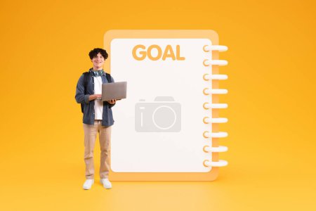 Photo for Smiling young caucasian guy student in casual use laptop for study near big list goal with free space, isolated on yellow studio background. Study, day planning, dream motivation - Royalty Free Image