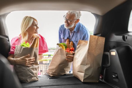 Photo for Loving attractive caucasian elderly couple putting food into car with open trunk, senior man and woman husband and wife load grocery packages in auto, shot from inside vehicle - Royalty Free Image