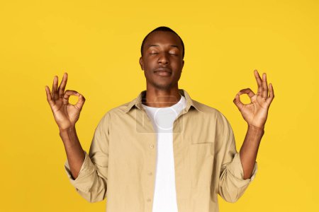 Photo for Calm millennial african american guy in casual with closed eyes, meditation, enjoy silence, isolated on yellow studio background. Emotions, ad and offer, break, health care, breathing exercises - Royalty Free Image