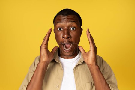 Photo for Shocked millennial african american man in casual with open mouth raises hands, screaming, isolated on yellow studio background. Surprise, stress, fear human emotions, ad and offer - Royalty Free Image
