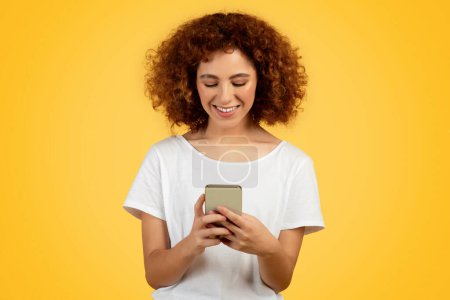 Foto de Mujer adolescente profundamente absorto en vibrante chat en el teléfono, aislado en el fondo amarillo, estudio, que refleja la era de la comunicación digital moderna y juvenil. Redes sociales, blog de aplicaciones - Imagen libre de derechos