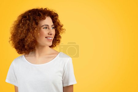 Photo for Smiling pretty teen woman in white t-shirt expressing happiness and vivacity, look at free space, isolated on yellow background, studio, close up. Student enjoy youthful, lifestyle - Royalty Free Image