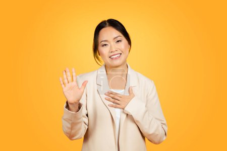 Photo for Capturing moment of bold sincerity, an Asian millennial woman raises her hand to swear or make pledge, on vibrant, attention-grabbing orange background in studio. Expression people - Royalty Free Image