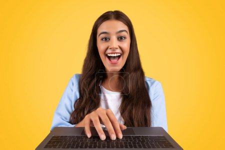 Photo for Cheerful european lady student with open mouth, typing at keyboard laptop, isolated on yellow studio background. Education, online lesson, surprise education project remote, video call with teacher - Royalty Free Image