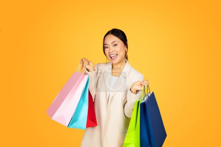 Photo for Joyful Asian millennial woman on shopping spree, her arms brimming with colorful bags, reflecting both delight of purchases and contemporary, consumer-oriented lifestyle of young adults today - Royalty Free Image