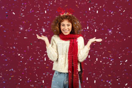 Photo for Glad spirited european teen woman, gleefully surrounded by shimmering confetti, as celebrates festive cheer of Christmas, eagerly anticipates arrival of New Year, isolated on red studio background - Royalty Free Image