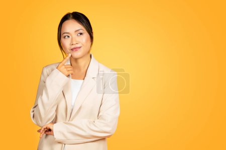 Téléchargez les photos : Contemplative jeune femme asiatique, encapsulée dans la pensée, dégage un comportement tranquille au milieu isolé sur fond jaune, studio. Expression réfléchie, peut-être résoudre ou réfléchir profondément - en image libre de droit