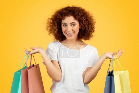 Téléchargez les photos : Joyeux adolescent femme joyeuse shopaholic, avec des sacs à provisions colorés, isolé sur fond jaune, studio, incarnant le plaisir de la jeunesse et le bonheur du consommateur. Acheteur avec achats - en image libre de droit